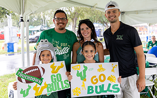 Group photo from tailgate with 3 adults and 2 children holding signs that say "Go Bulls"