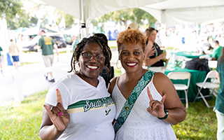 two women at the tailgate giving the horns up hand gesture
