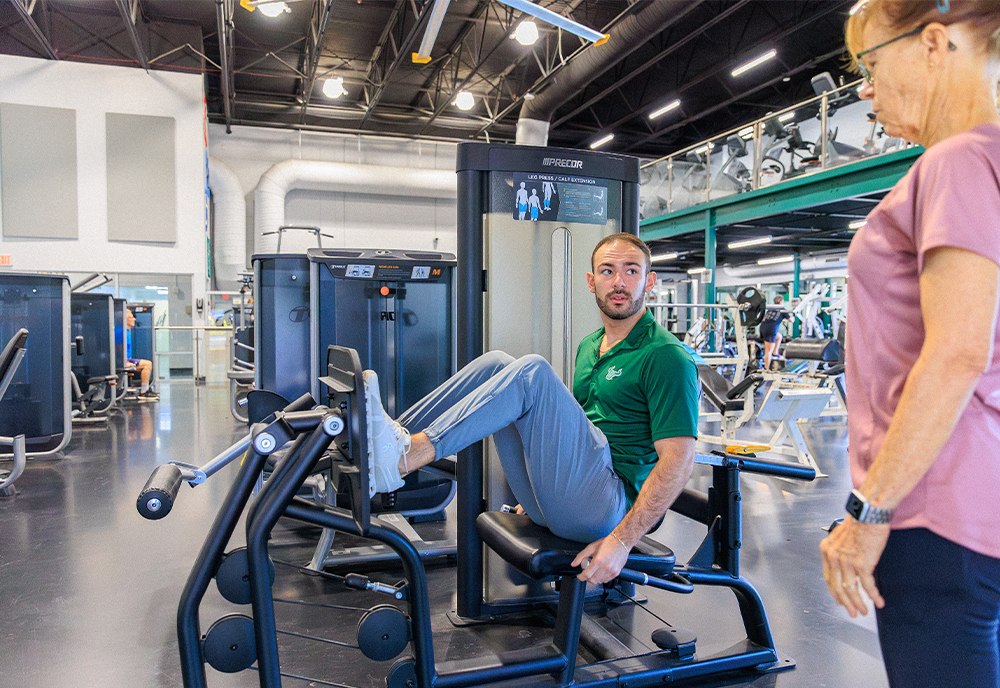 Student showing woman how to use machine inside the gym