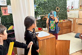 3 preschool students playing with an old camera