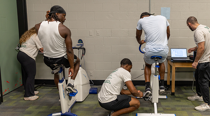 multiple students helping while two athletes are on stationary bikes