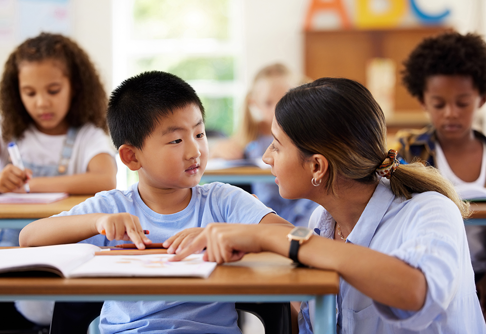 Teacher talking to young student in classroom