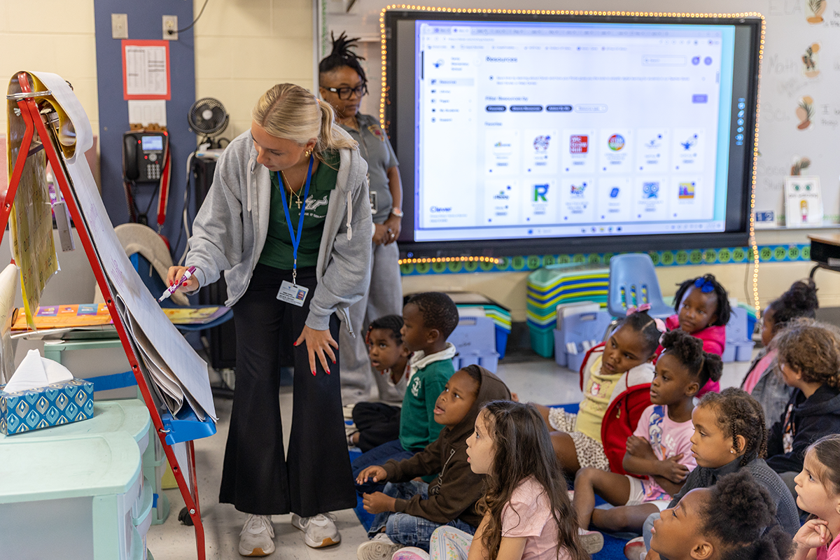 teacher leading classroom with screen on behind her