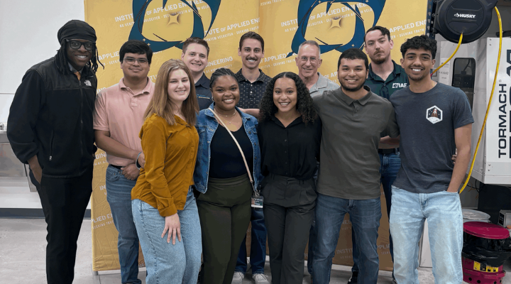 Group of interns posing in front of yellow IAE banner