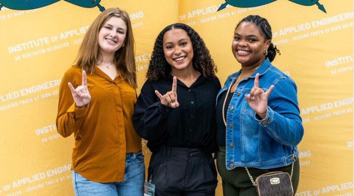 Group of students holding up a Bulls sign in front of yellow banner