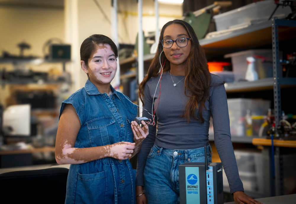 Two students posing for a photo and holding a listening device in an engineering lab