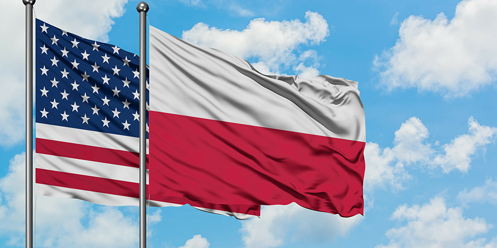 Flags of the USA and Poland waving in the breeze against a blue sky background with white clouds