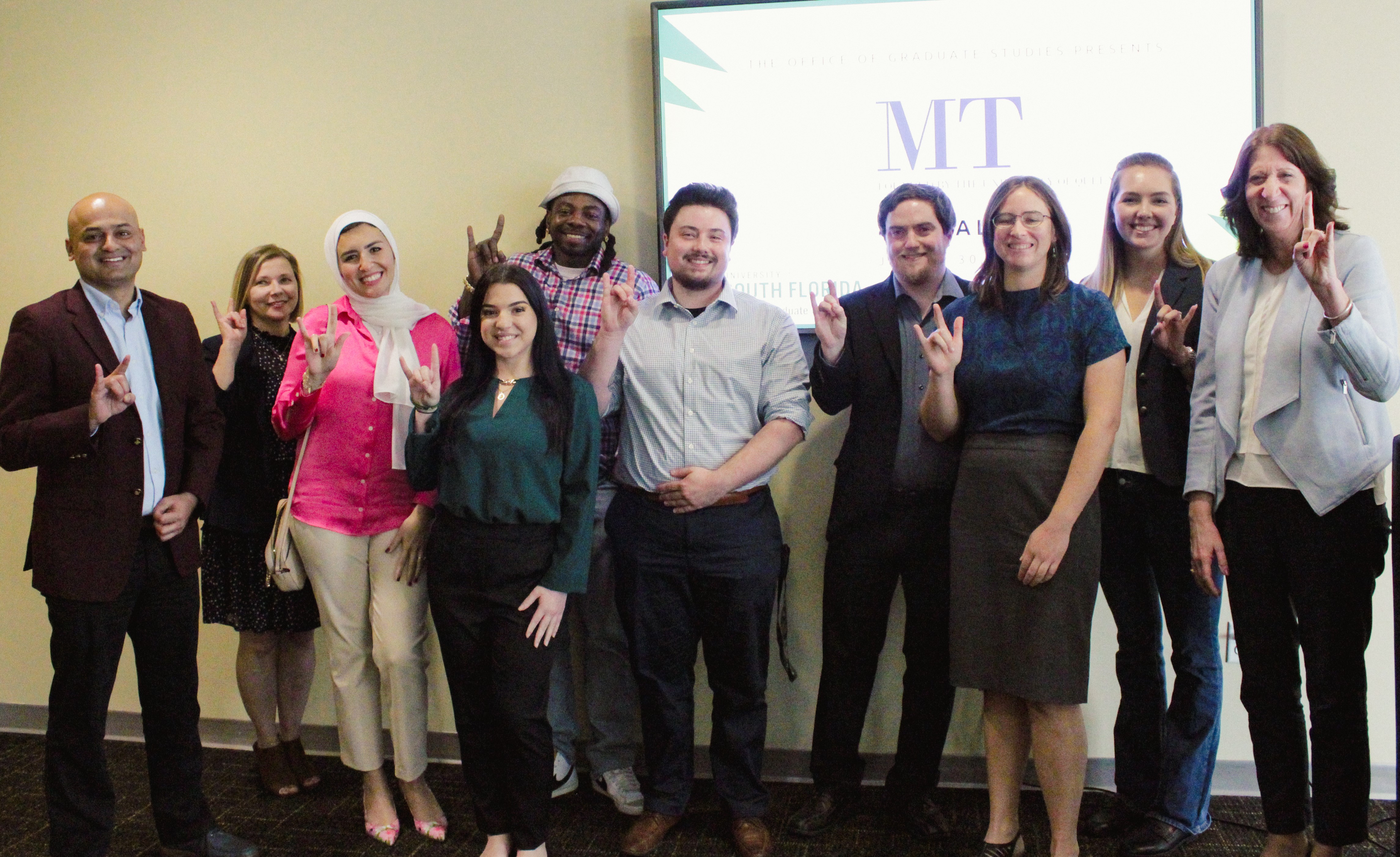 3MT participants pose with Dean Ruth Bahr while holding hands up in the shape of a Bull