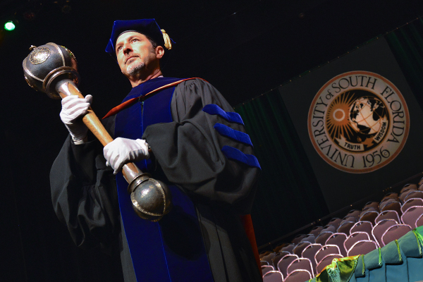 Faculty member holding MCOM mace.