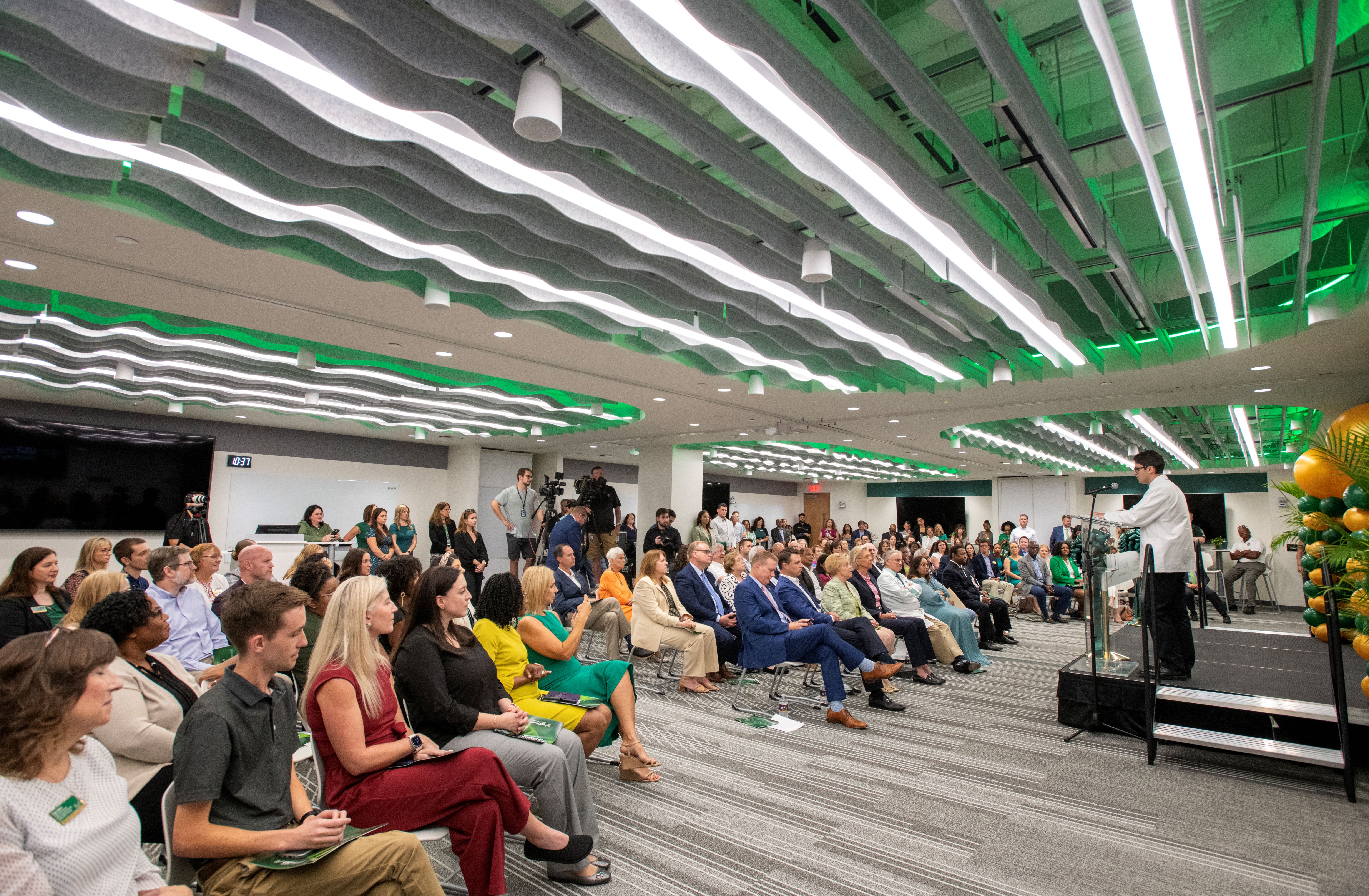 Fourth-year pharmacy student Joseph Diamond addresses a full classroom at the ribbon-cutting ceremony.
