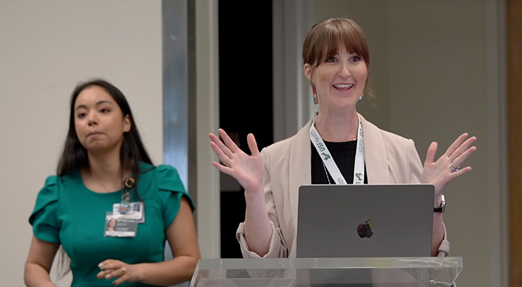 Dr. Stephanie Watts gestures with her hands in front of a lectern to a class.