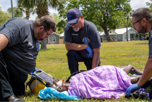 Three emergency medical providers outside, training a simulation mannequin