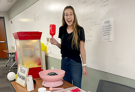 A woman smiles while holding cotton candy in a classroom with a white board.