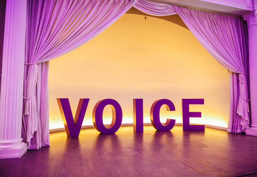VOICE in big block letters bellow a purple curtain