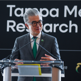 Dr. Haru Okuda speaking at a clear podium