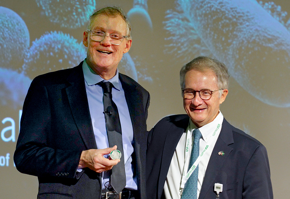 Dr. Stephen Liggett accepts the Culture Coin award from Dr. Charles J. Lockwood, executive vice president of USF Health and dean of the Morsani College of Medicine, during USF Health Research Day on March 6, 2026. The award recognizes Liggett's outstanding contributions to USF Health's research culture.