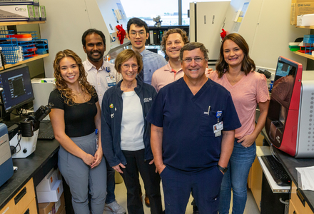 Research team members pose together in a biomedical research laboratory surrounded by scientific equipment and workstations.