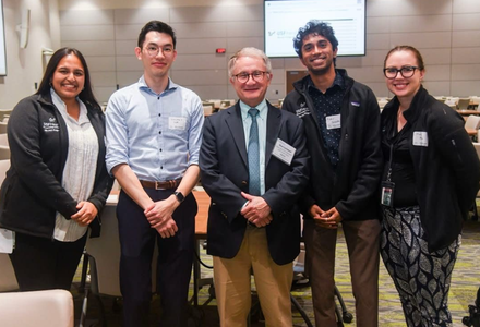 Five attendees pose together at a professional academic or research networking event in a conference setting.