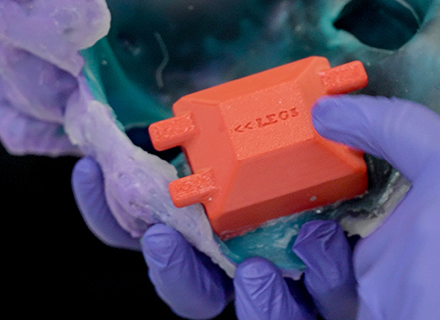 A blue-gloved hand handles a red cradle. 
