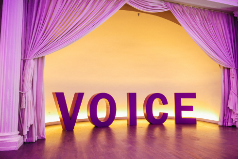VOICE in big block letters bellow a purple curtain