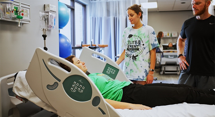 Two people looking at a patient in a hostpital bed