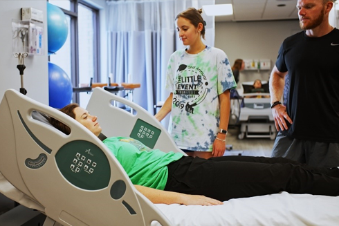 Two people look at a patient in a hospital bed