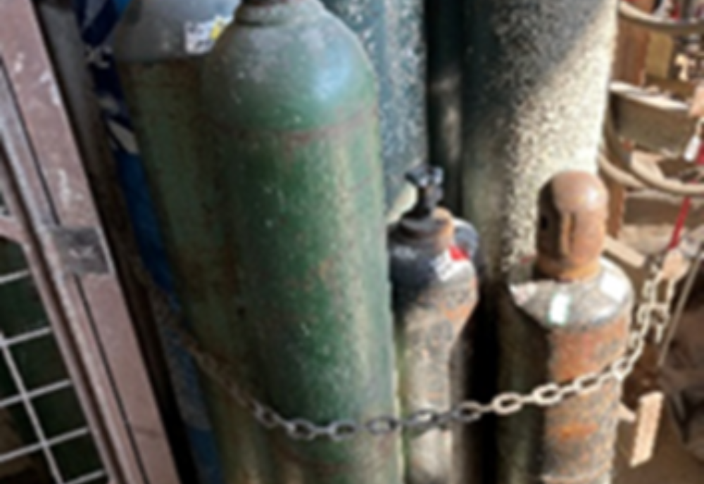 An oxygen cylinder is stored immediately next to a fuel-gas cylinder in a welding area.