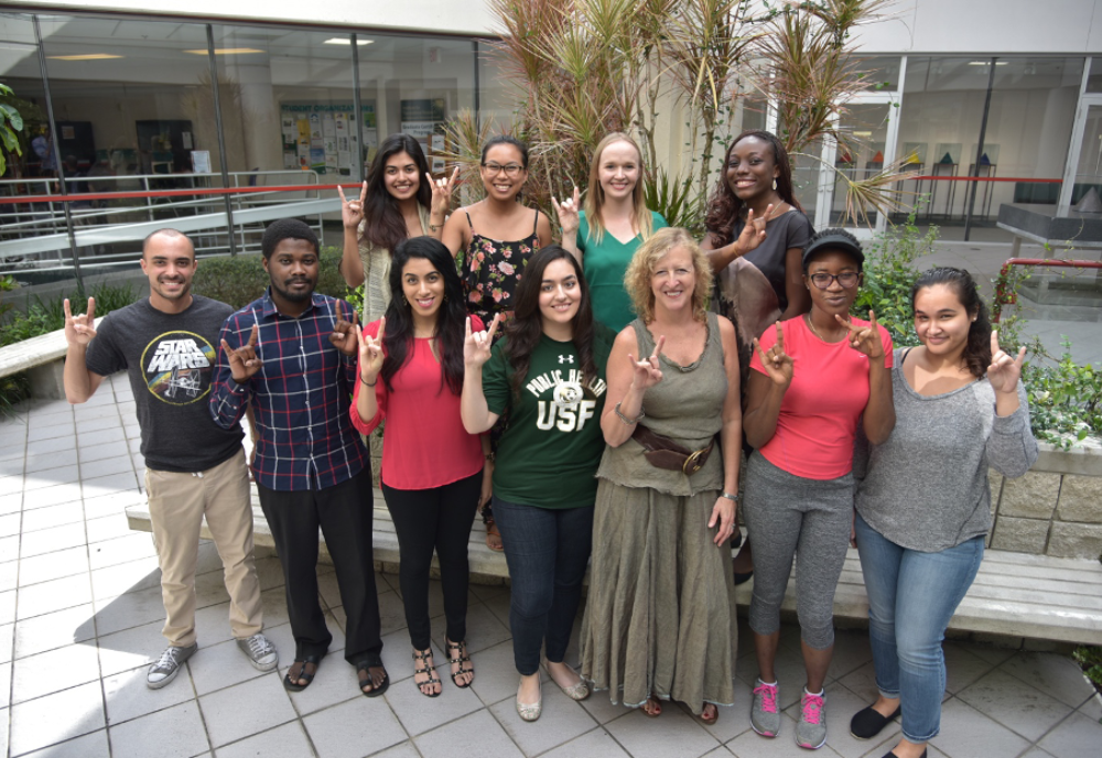 Dean Petersen standing with group of students outside flashing USF Bulls hand sign.