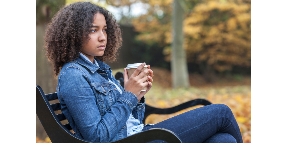 Black female teen sitting on park bench looking sad