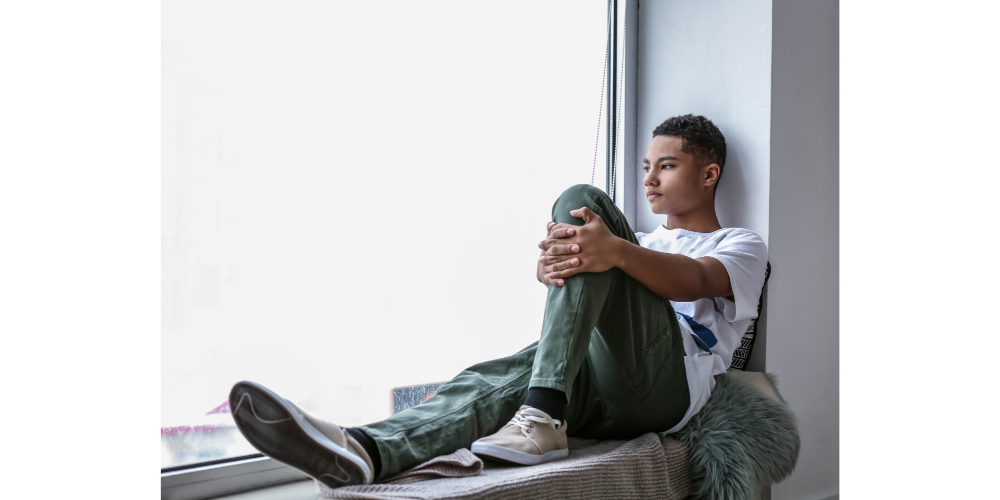 Black teen looking out window looking sad