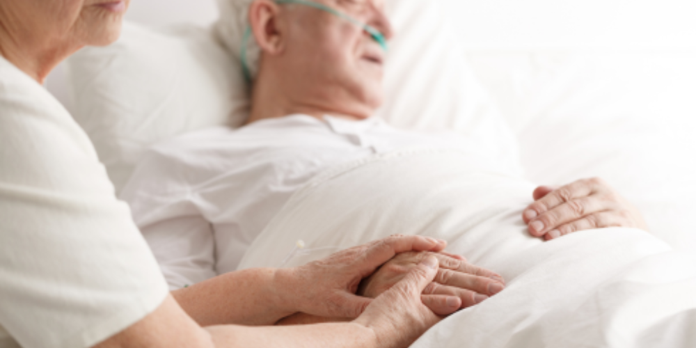 Older man in hospital bed and older woman holding his hand