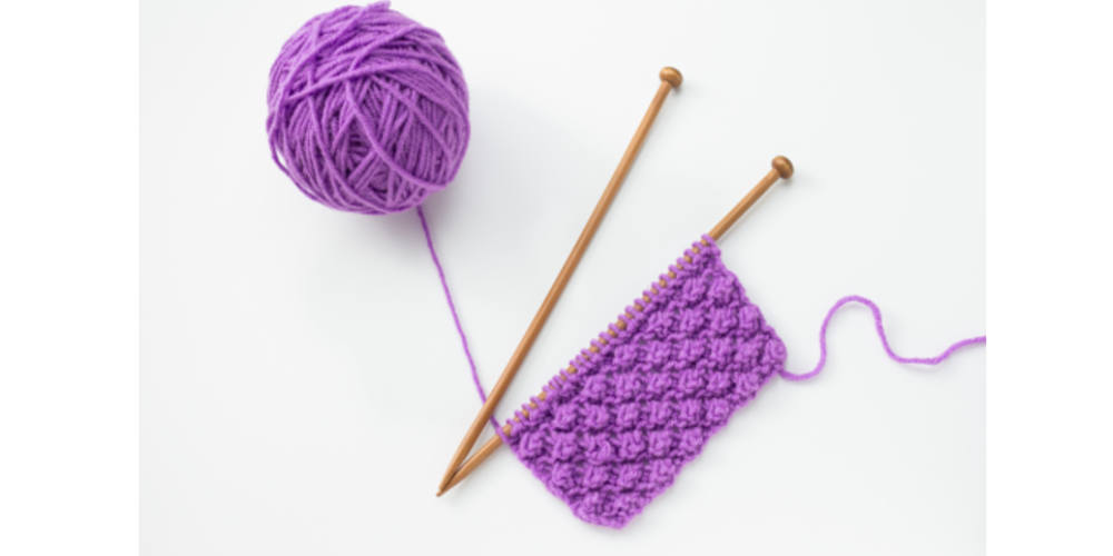 purple ball of yarn with purple stitching and knitting needles