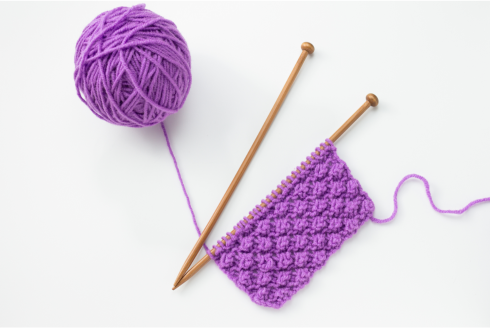 ball of purple yarn and knitting needles and small patch of knitting