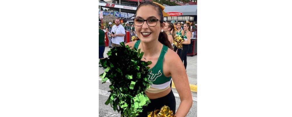 young woman with glasses holding green and gold pompoms