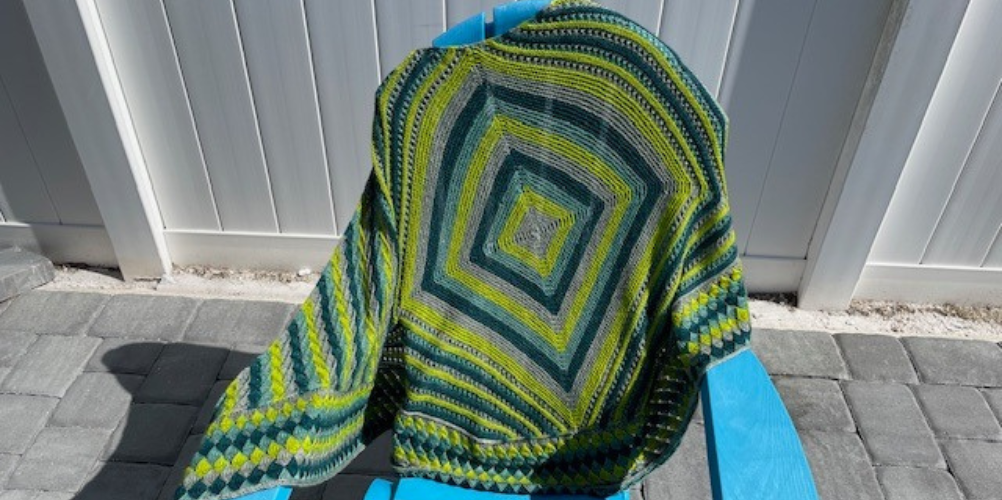 blue and green knitted shawl draped over a chair outdoors