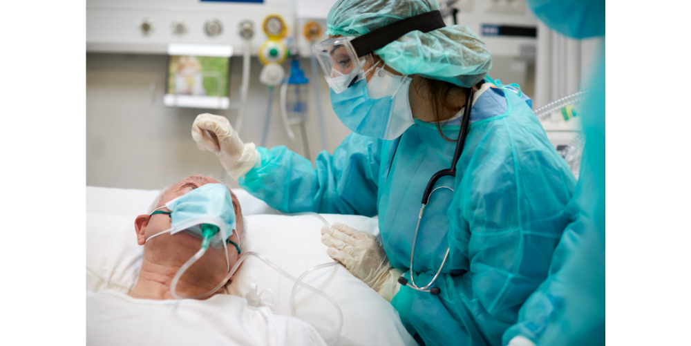 nurse wearing protective gear caring for patient in hospital bed