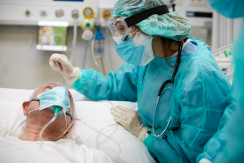 health care worker in protective gear tending to patient with mask in a hospital bed