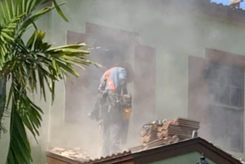 A worker is cutting roof tiles under a cloud of dust.
