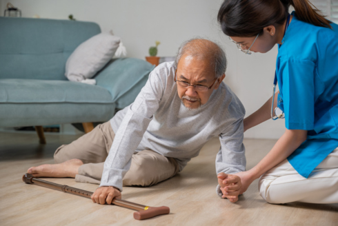 An elderly Asian man falls to the floor as a compassionate nurse rushes to assist him in a nursing home.