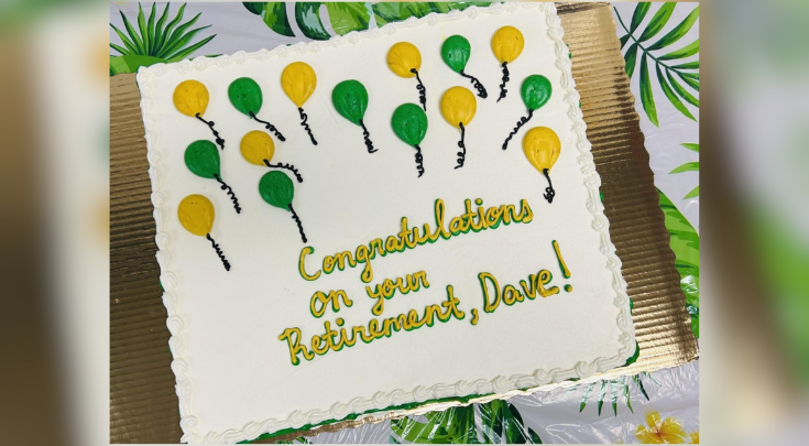 A white cake with yellow and green icing. "Congratulations on your retirement, Dave!"