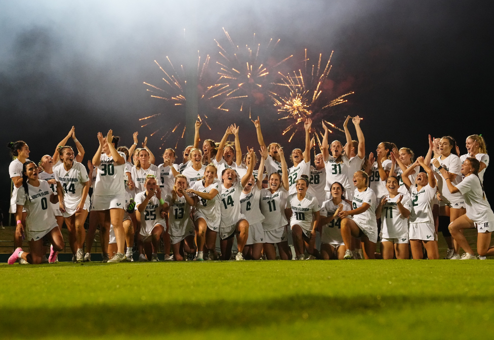women's lacrosse team in front of fireworks