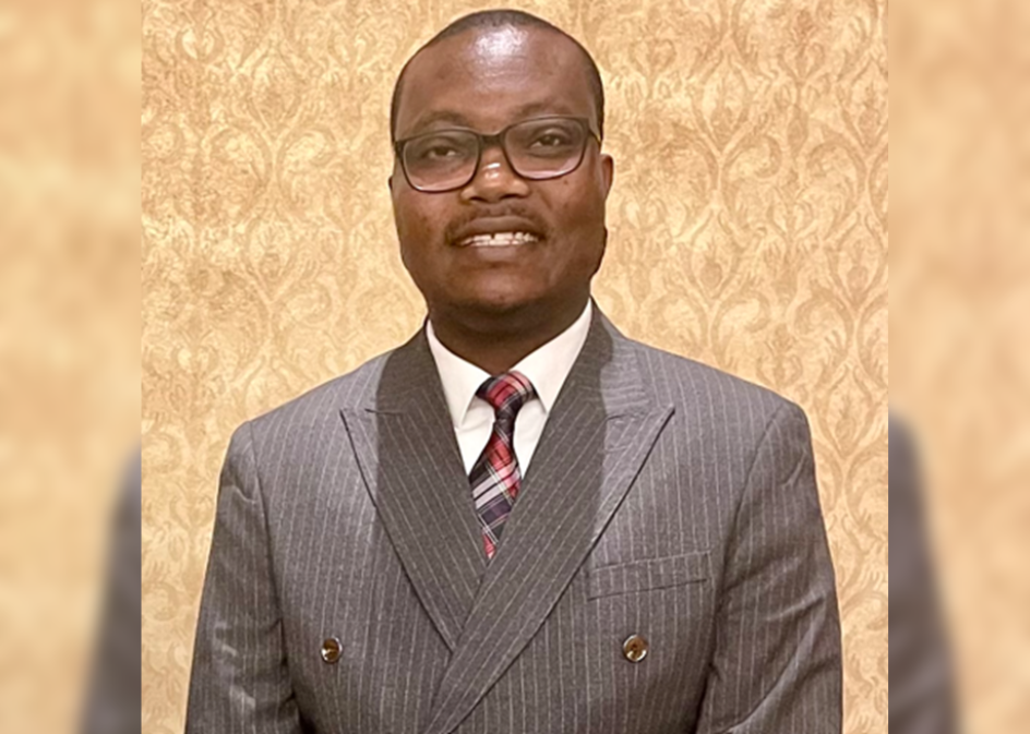 Aihinoria Joseph Olisa smiling in front of a beige wall.