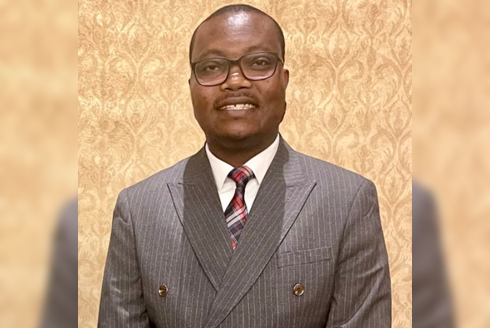 Aihinoria Joseph Olisa smiling in front of a beige wall.