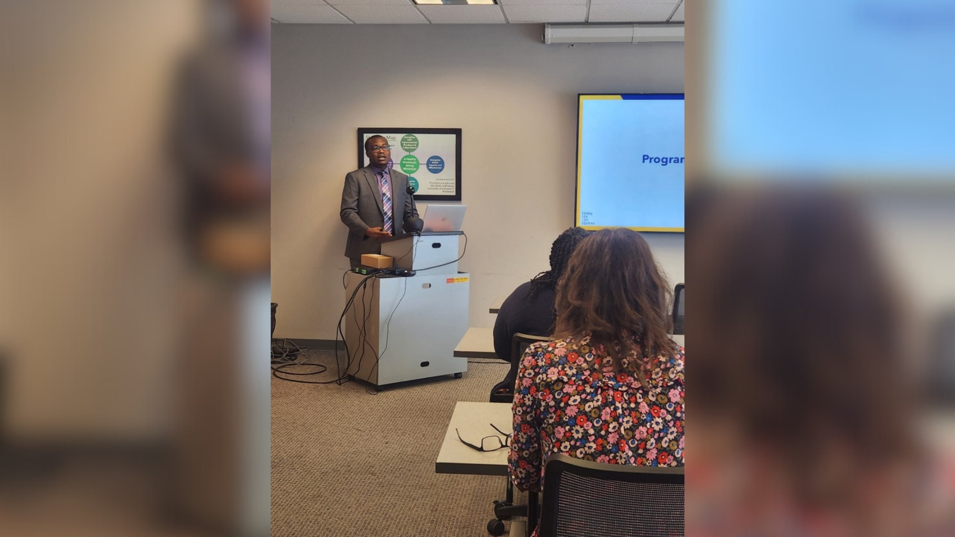 Aihinoria Joseph Olisa presenting in front of a room of people.