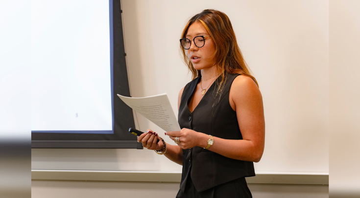 A young woman reading off a sheet of paper.