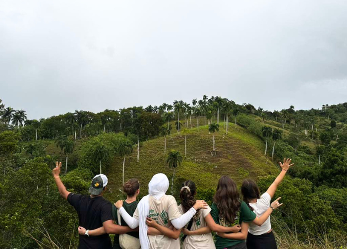A group of six students facing away from the camera towards the tree-filled landscape in front of them.