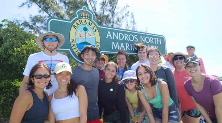 A group of Honors students pose in the Bahamas by a sign that reads "Andros North Marine Park"