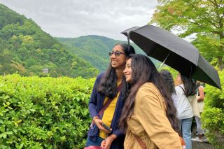 Two Honors students hiking in lush green hills with a black umbrella
