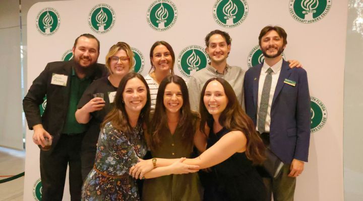 Honors alumni pose in front of USF Judy Genshaft Honors College step and repeat poster