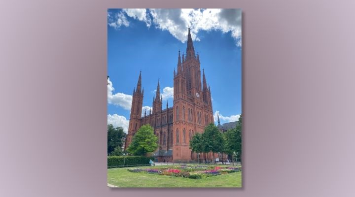 A photo of a church steeple with a bed of flowers in front